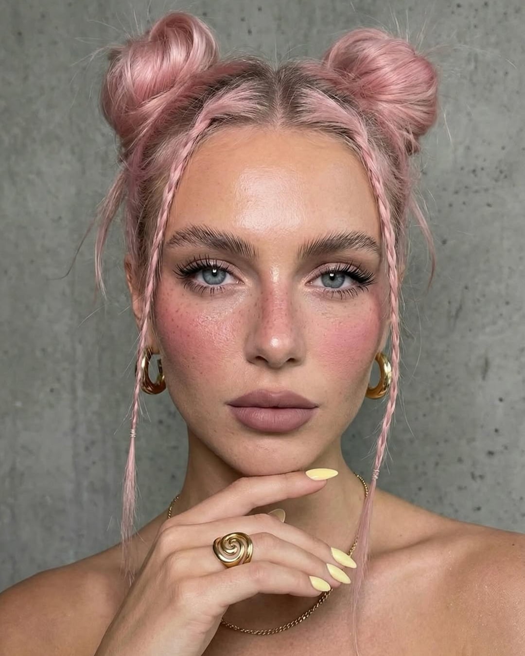 Woman with pastel pink hair in high space buns with face-framing accent braids