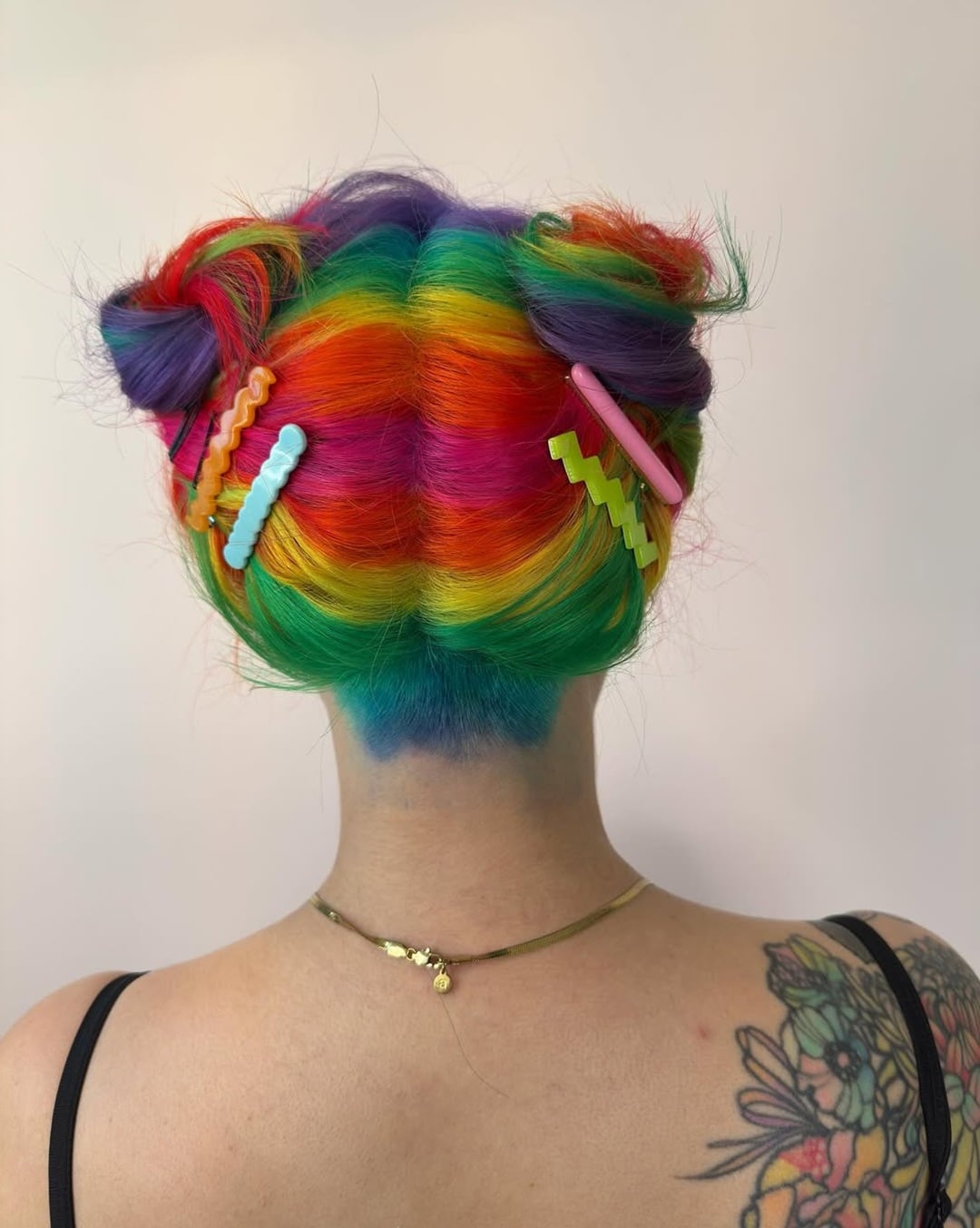 Vibrant rainbow hair styled into twin space buns with colorful hair clips