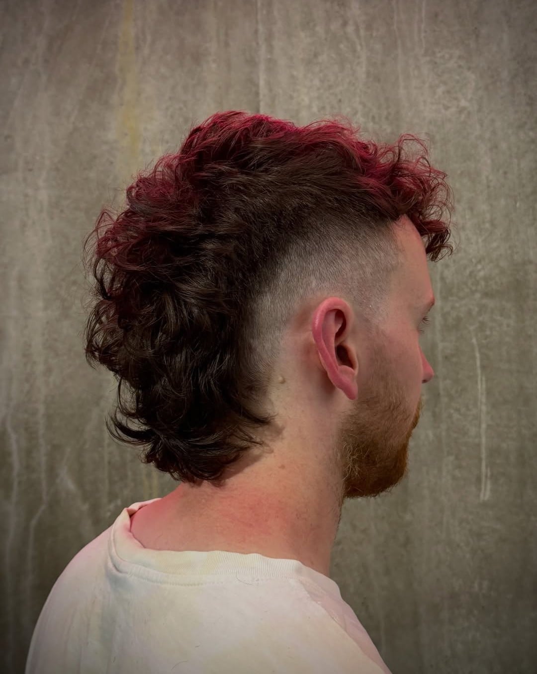 Wavy mohawk with deep red tips and a burst skin fade around the ear