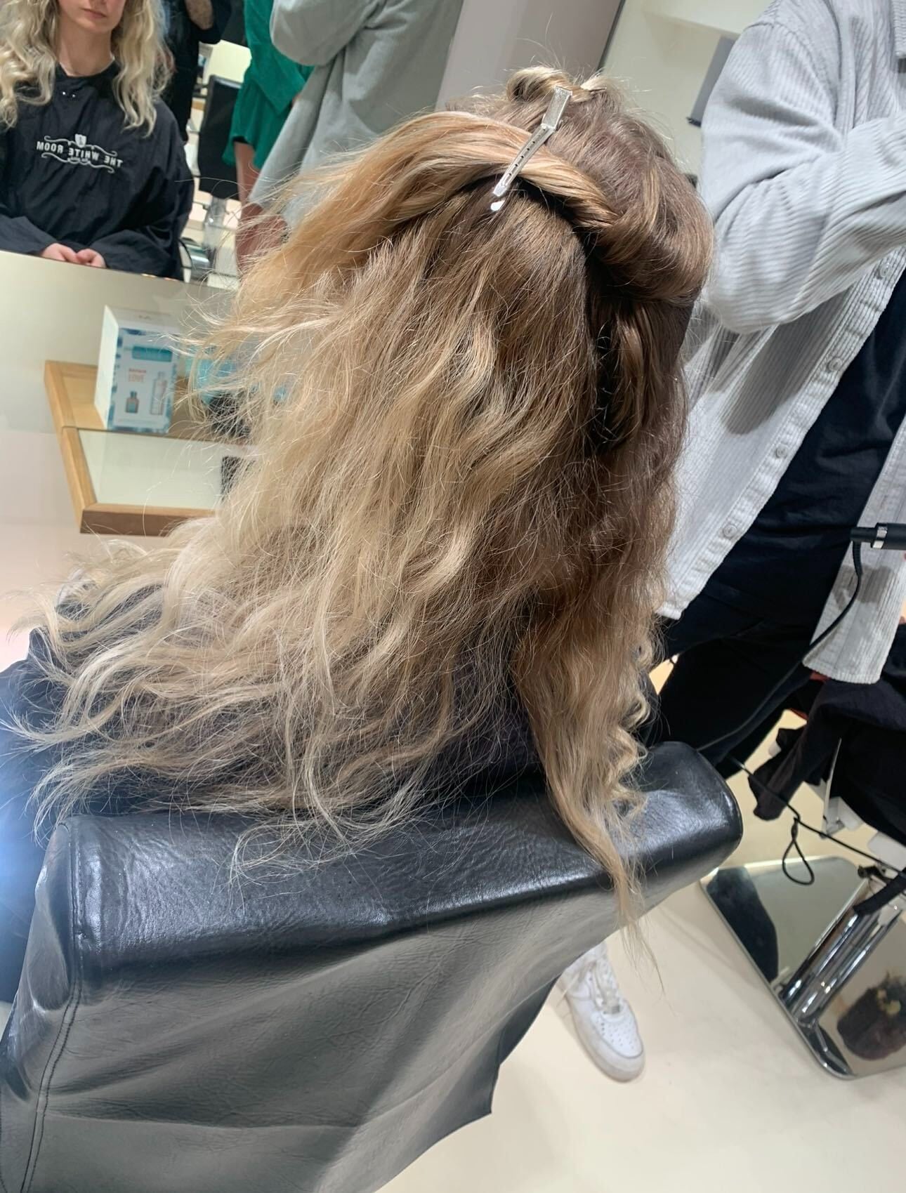 Back view of a client in the salon chair with the top sections of wavy blonde hair twisted up and clipped