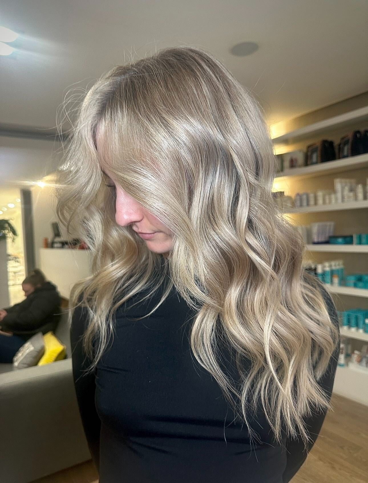 Client with long blonde hair styled in smooth loose waves with face-framing layers in the salon