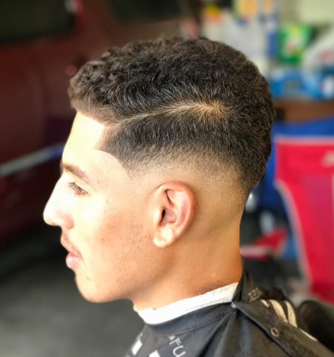 Side profile of a man with a short curly comb over haircut featuring a side part and clean mid skin fade