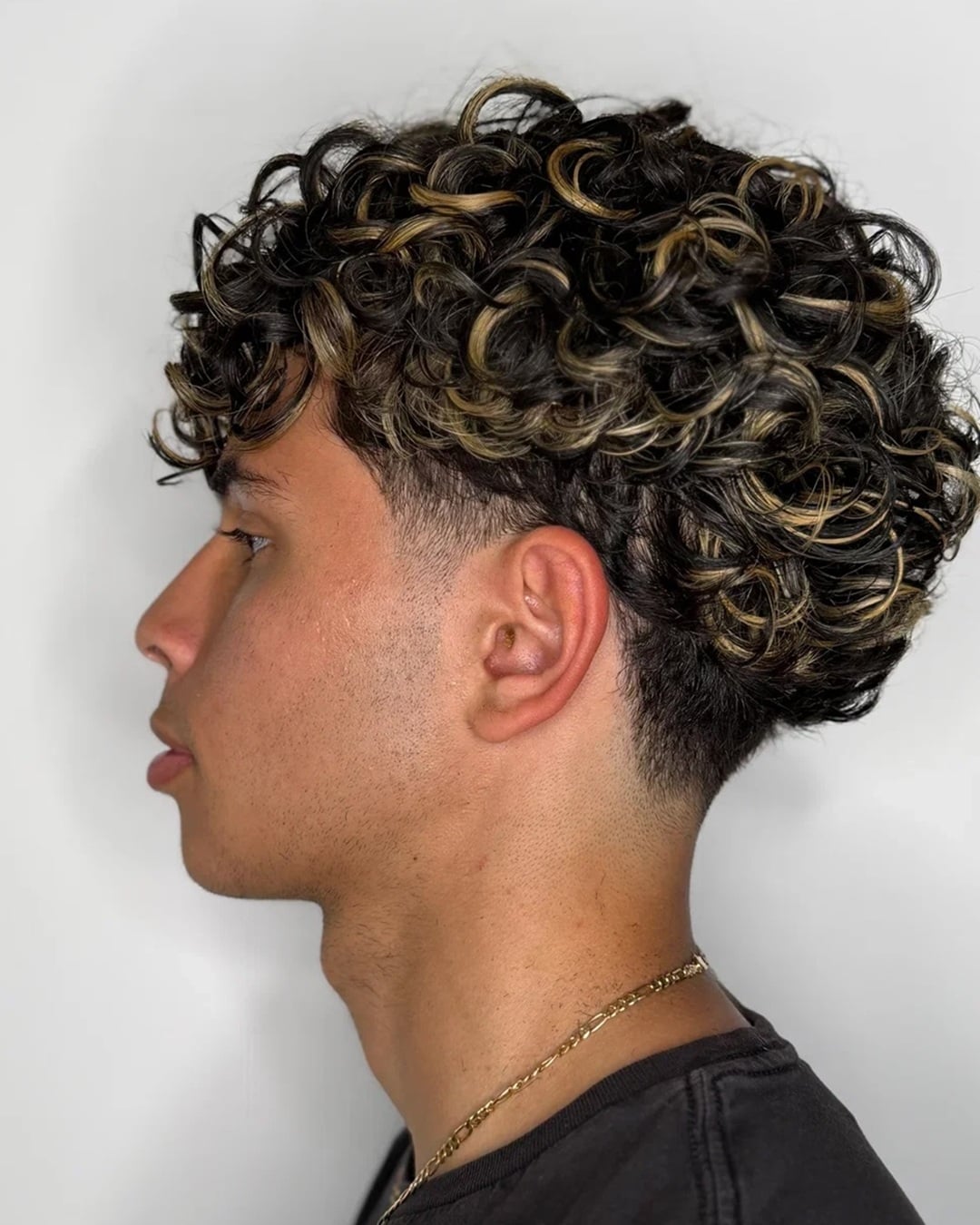 man with short dark curly hair featuring blonde highlights and a taper fade