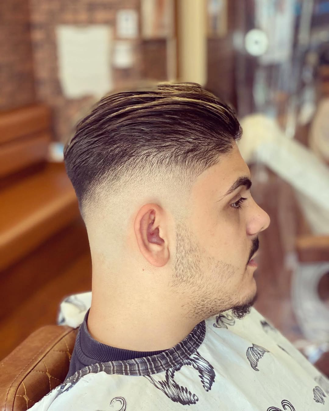 Man with a mid skin fade and slicked-back hairstyle featuring golden blond streaks
