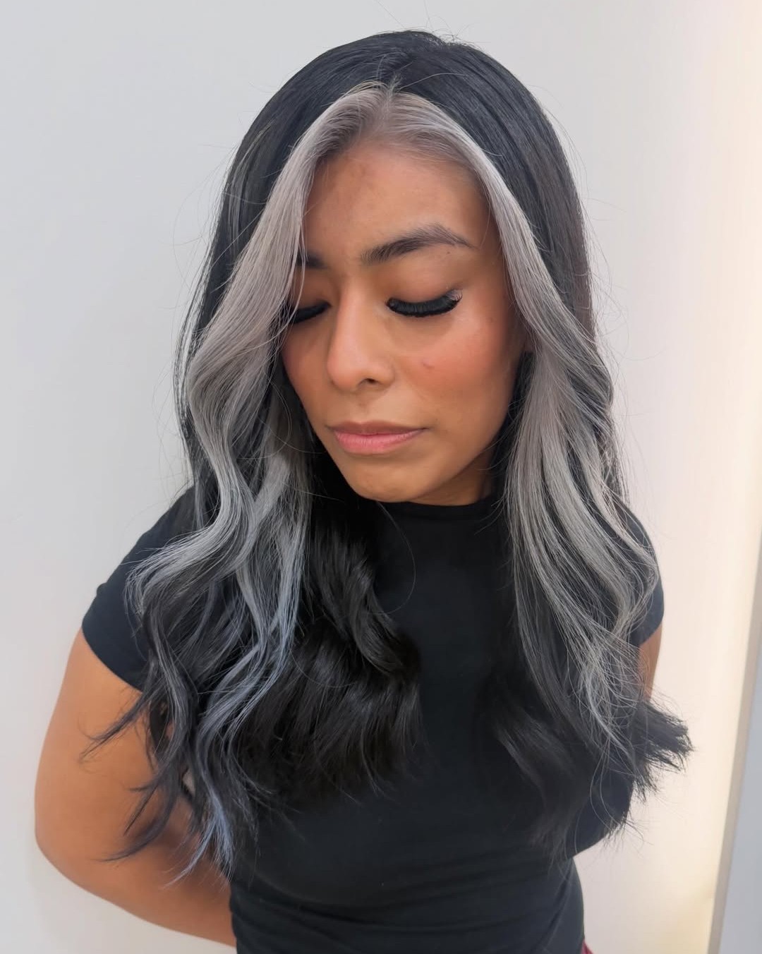 Woman with dark wavy hair featuring a smokey silver face framing money piece