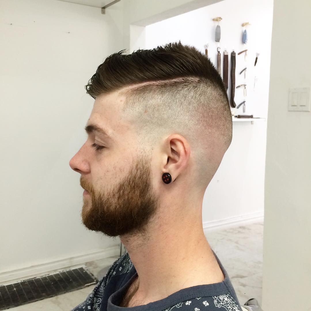 Man with a high skin fade, hard part line, textured spiky top, and full beard