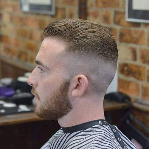 Side profile of a man with a clean taper fade haircut and groomed short beard framing his receding temples