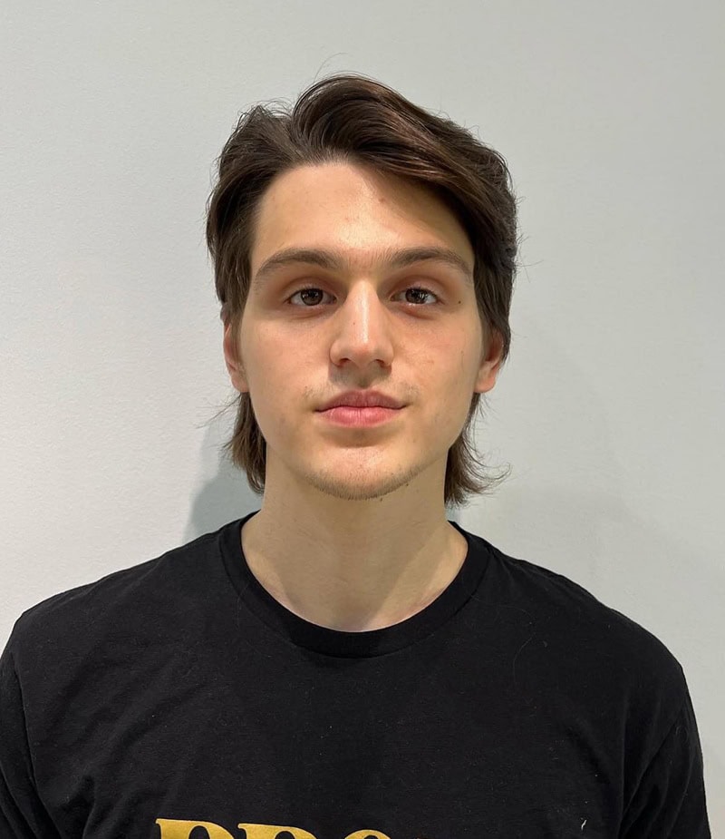 teen boy with dark, flowy hair styled in a deep side part