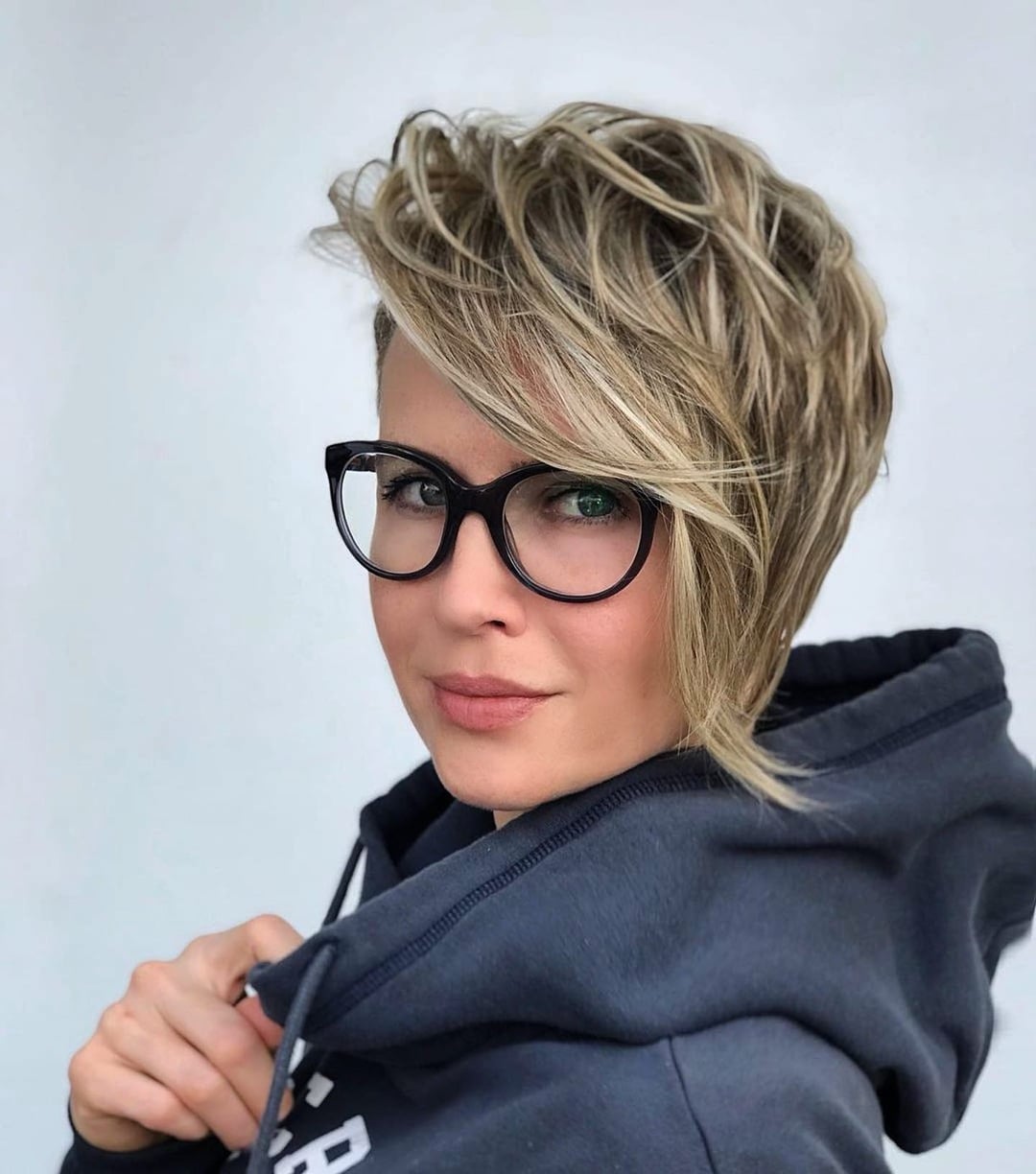 Blonde pixie with dark roots, lifted crown layers, and long, side-swept bangs