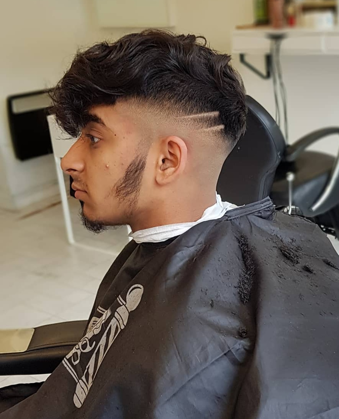 Young man with a wavy textured crop skin fade featuring double shaved design lines