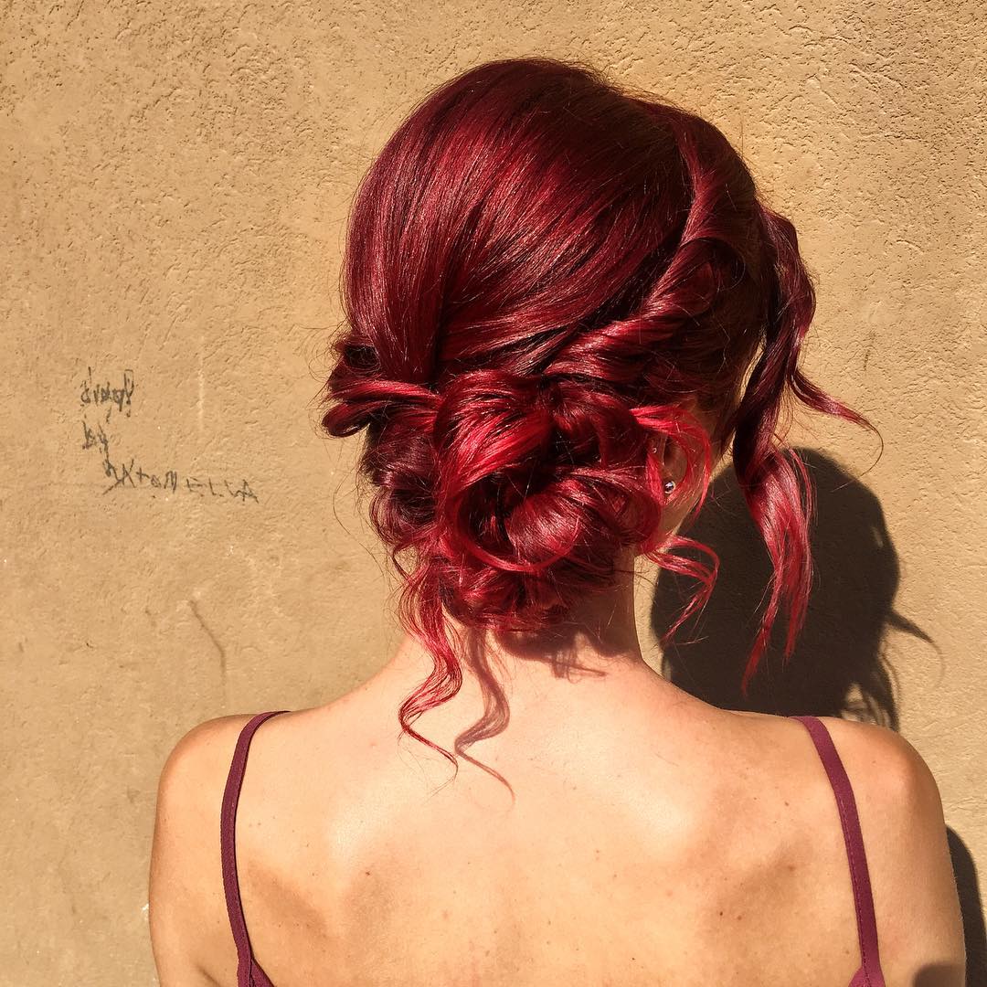 Back view of a woman with vibrant ruby red hair styled in a low messy bun featuring side twists and loose tendrils