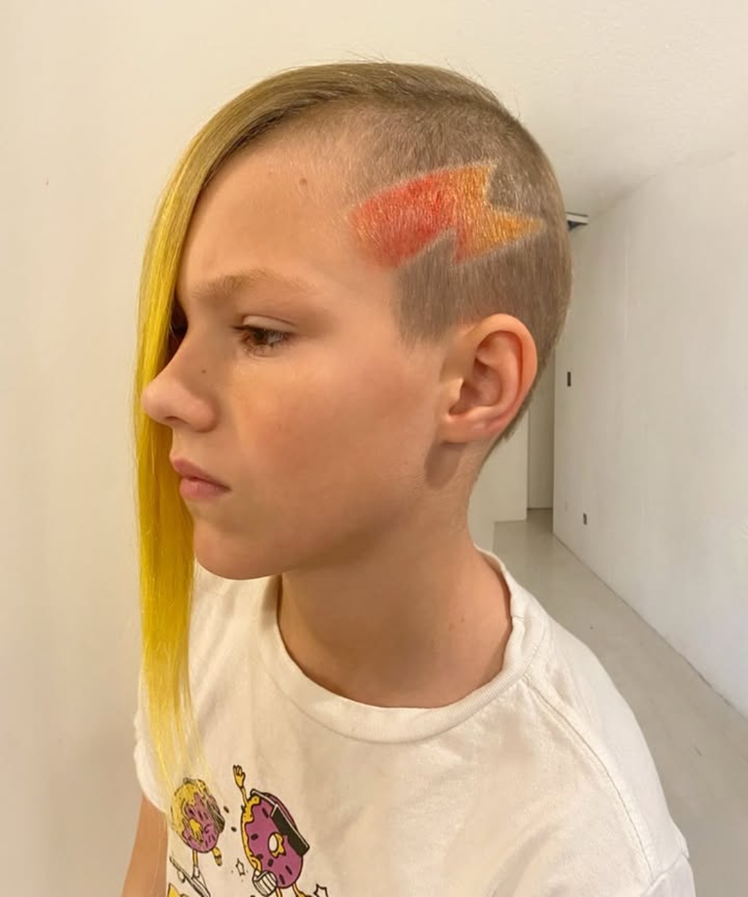 Boy with an asymmetrical haircut featuring long yellow hair and a colored lightning bolt hair design on the shaved side