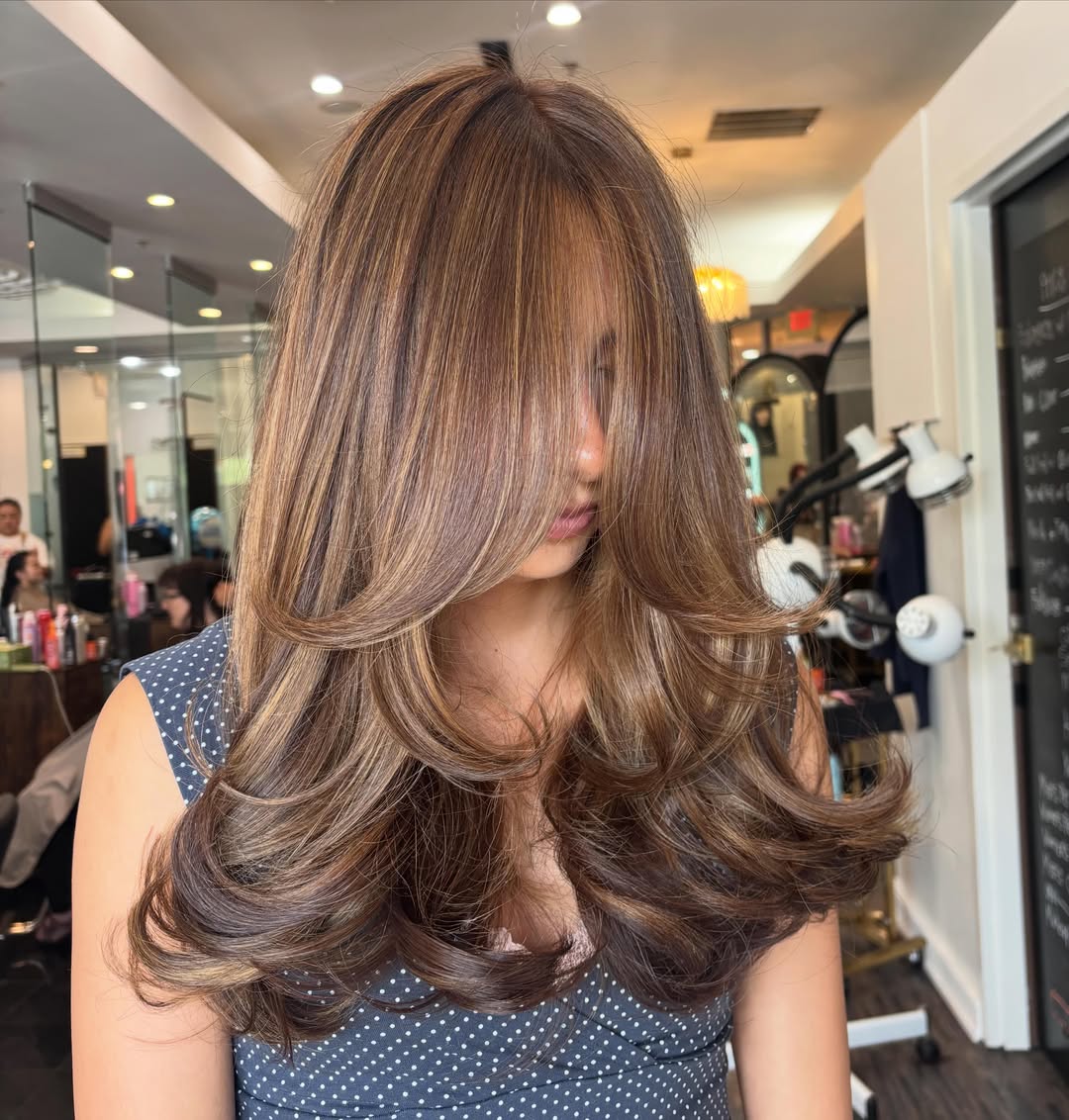 Woman showcasing a bouncy layered blowout with warm mousy brown hair color and caramel highlights