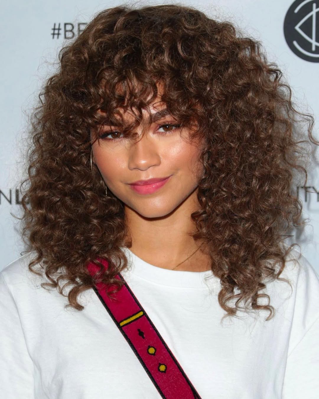 Zendaya featuring a voluminous shoulder length curly hairstyle with full curly bangs