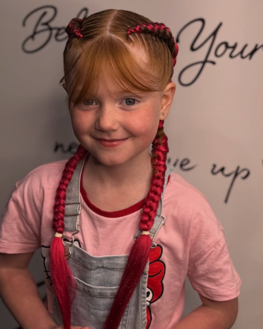 Young white girl with straight bangs wearing two braids styled with vibrant pink feed-in extensions.