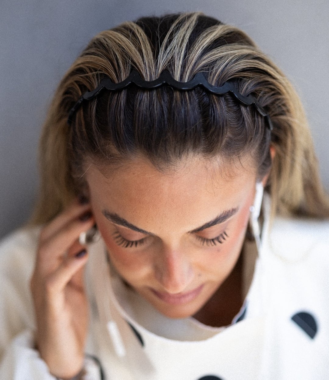 Woman wearing a black zigzag headband pulling back her highlighted hair